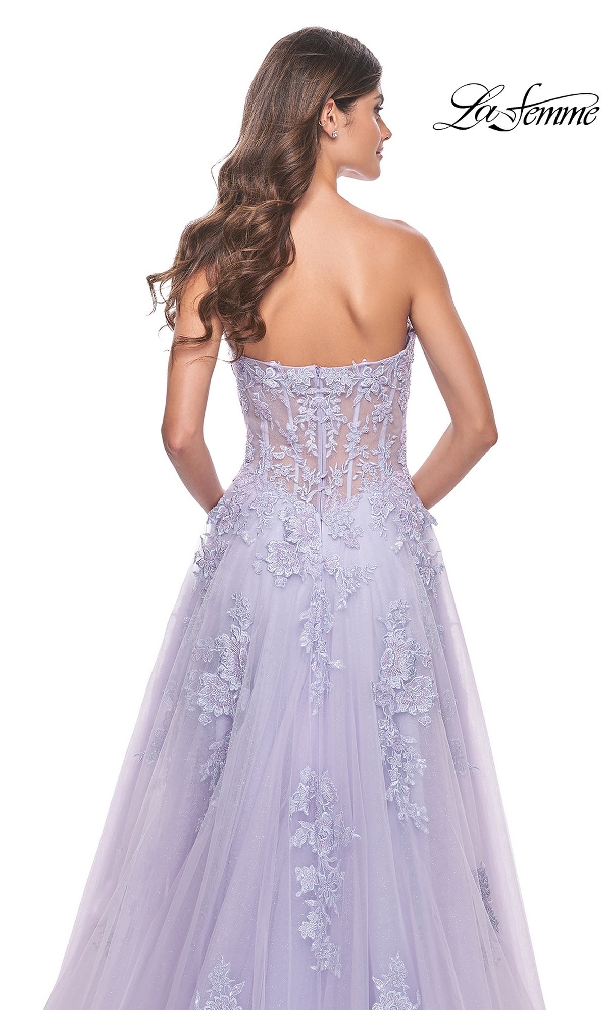 A woman with long wavy hair models the La Femme Strapless Long Lace Prom Dress 32145 in lavender, featuring a strapless sheer bodice and embroidered floral lace, shown from the back with the La Femme logo at the top right.